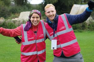 Marshalls at a park run - a woman on the left and a man on the right with their arms extended, wearing red high-vis jackets