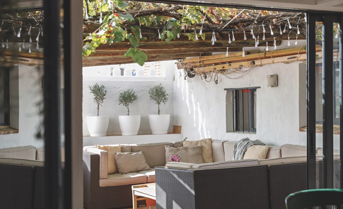 A photo of a living area with sofa surrounding a low coffee table. One wall and the ceiling has lots of plants