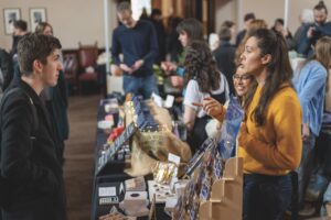 People standing at food stalls in a hall buying and selling