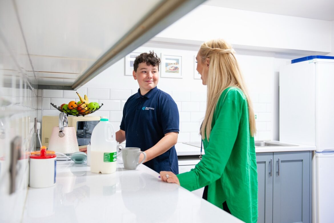 A teacher and student stand in a kitchen making a cup of tea