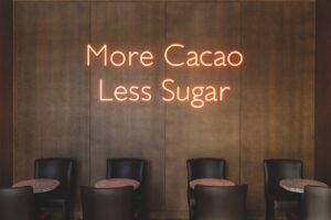 A wooden wall with a neon light that says "More Cacao Less Sugar" with tables and chairs below