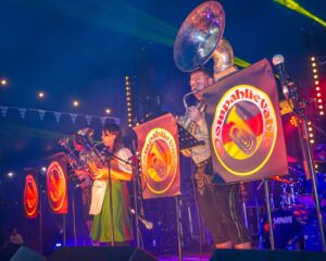 A group of people playing large brass instruments on a stage wearing dirndl and lederhosen