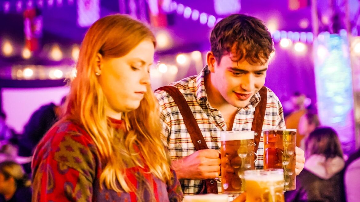 Two people holding large mugs of beer inside a tent