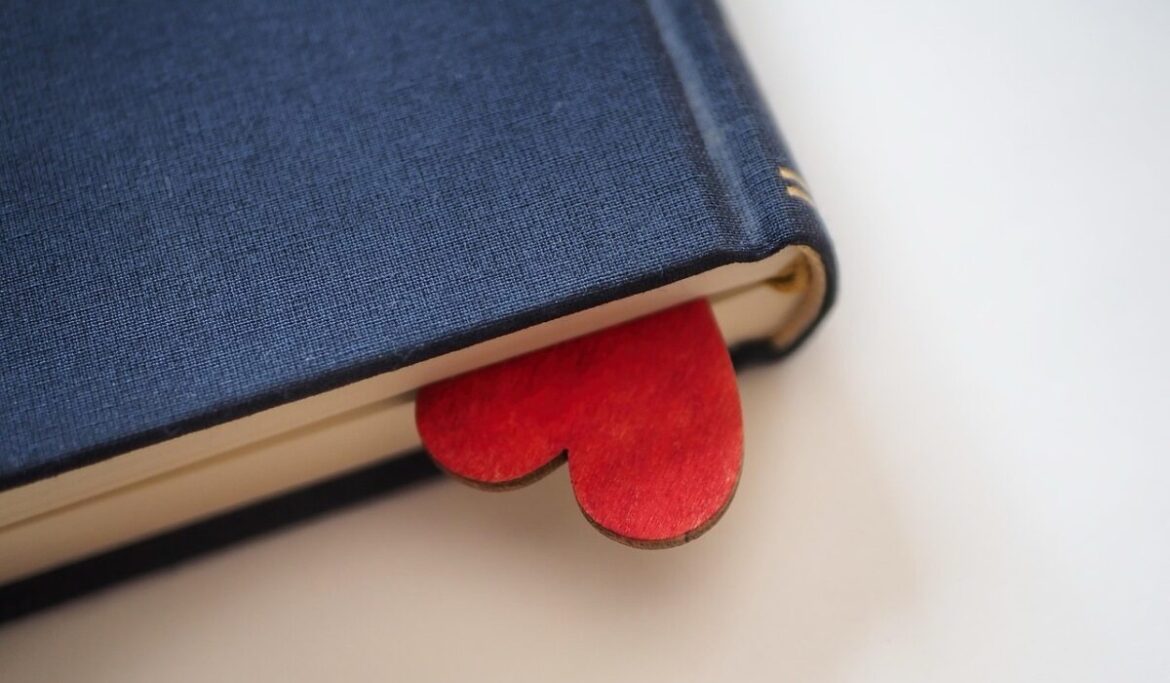 A closed blue book with a red heart hanging out of it