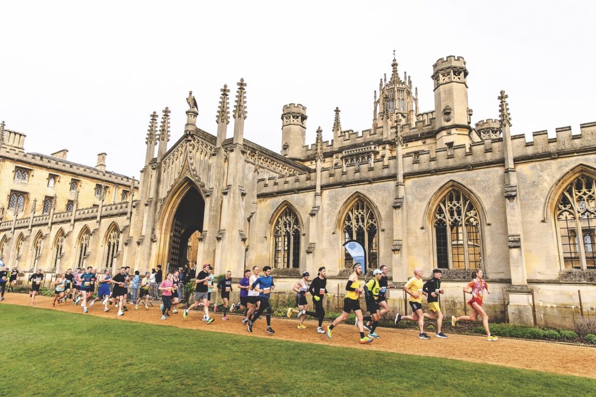 People running in front of an old ornate building, St Johns College in Cambridge