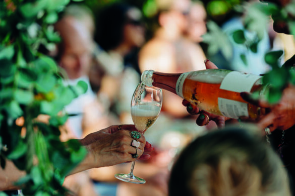 A hand pouring wine into someone's glass. There are more people sitting in the blurred background