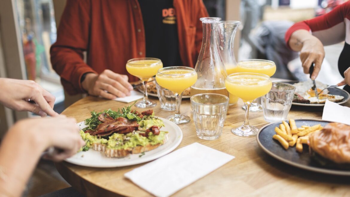 A table with people seated around eating brunch. There are plate sod food, cups of water and glasses of orange juice. Image by Ian Olsson