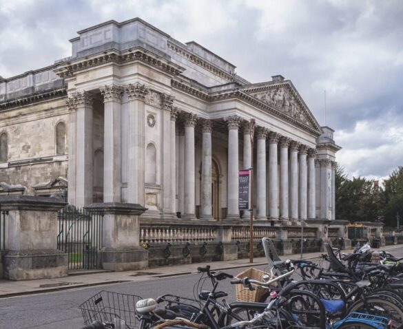 A large white building with long columns and a fence. A line of bikes are parked opposite it