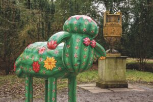 A green sheep statue standing near an old trophy statue