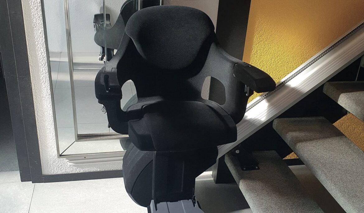 A black stairlift chair sitting in front of a mirror at the bottom of the stairs