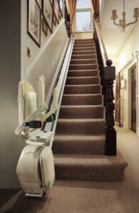 A long flight of stairs with a white, modern stairlift seat sitting at the bottom