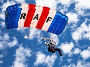 A person glides to the ground with a large red, white and blue RAF parachute. They are against a blue sky with lots of small, white clouds