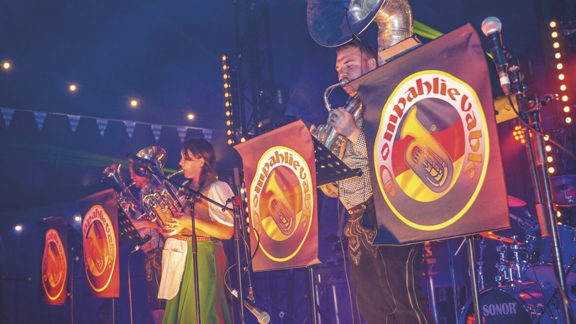 A band stands in traditional dress with large brass instruments on a dimly lit stage