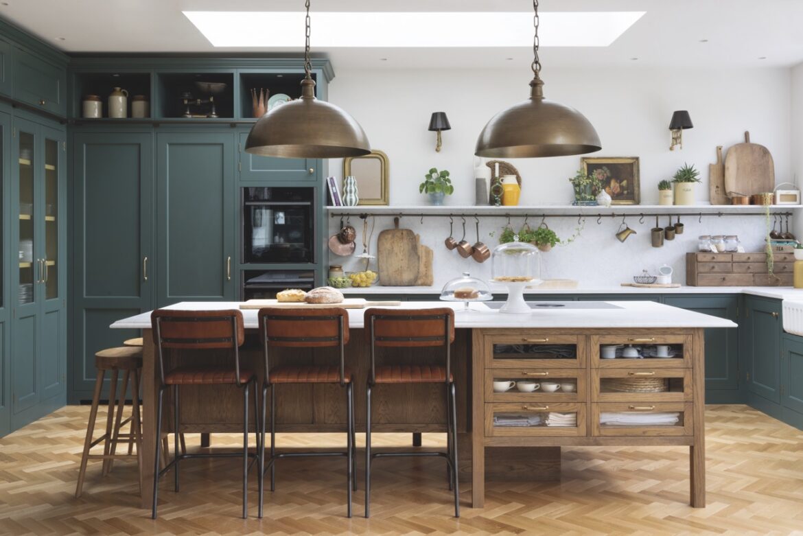 A modern kitchen with bronze hanging lights, olive walls and a large table with chairs