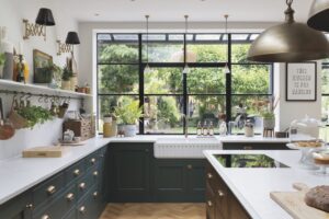 A modern kitchen with a large window. The counters are grey and white, and shelves line the room