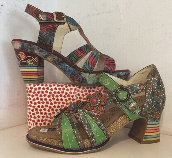 Two patterned green heeled shoes. One is raised on a red dotted block