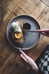 A top view of a grey plate with a poached egg on bread and black sauce on. A knife and fork cut into the meal