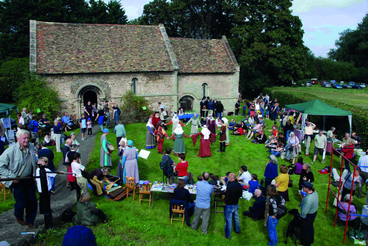 A small chapel with a crowd standing outside. Some of the people stand in a circle in period dress