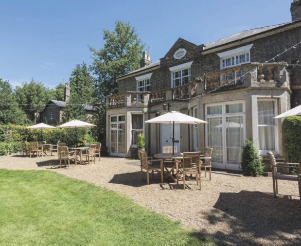 An outside seating area for a pub. There are tables with umbrellas and a small area of grass