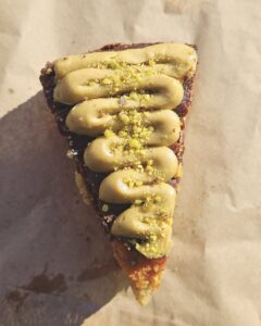 Top view of a slice of cake on baking paper with cream piped on and pistachio sprinkled on top