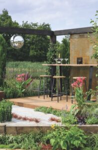 A modern garden with a wooden seating area and a black frame with a mirrored ball hanging from it