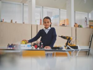 A young girl in school uniform standing in science lab with a bee robot