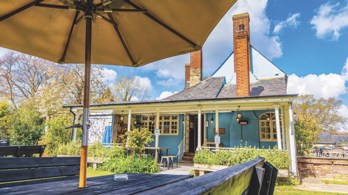 An outdoor seating area with a bench and umbrella. There is a building with tall chimneys in the background