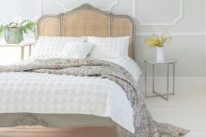 A double bed with white and floral bedding draping on the floor in a white room