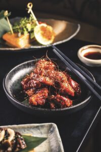 Chicken coated in red sauce and saffron on a black plate
