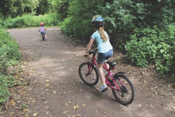 A young girl cycles after a boy on a bike on a path in a forest area