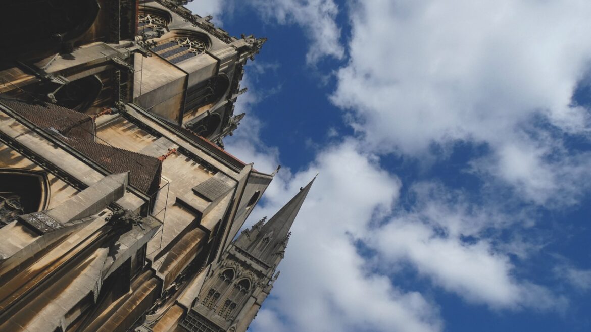 A low view of an old building with spires and towers. The sky is blue and cloudy