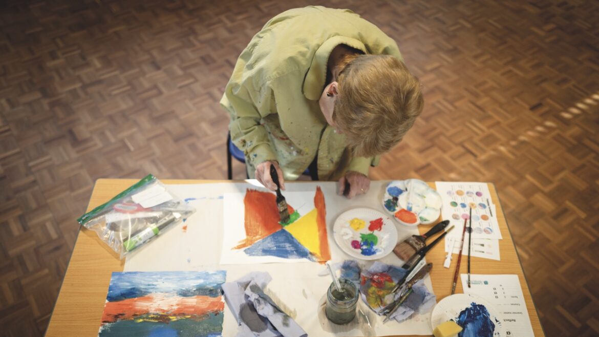 A person sitting at a table painting and drawing with bright colours