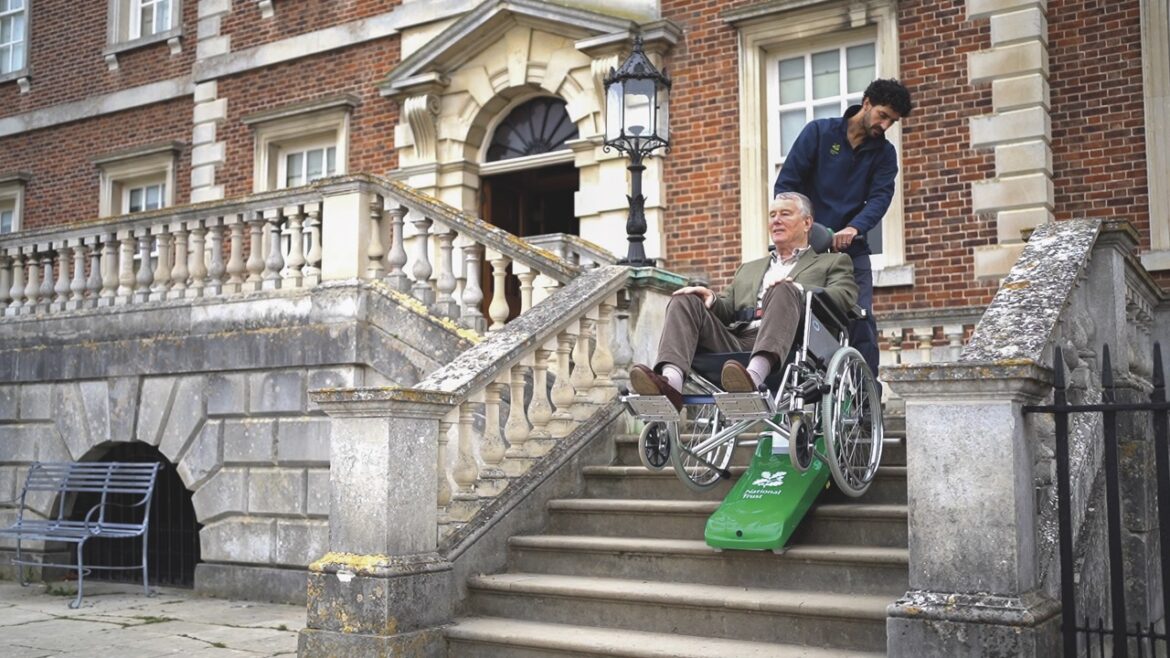 A man pulling a man in a wheelchair up the steps of an old stately home