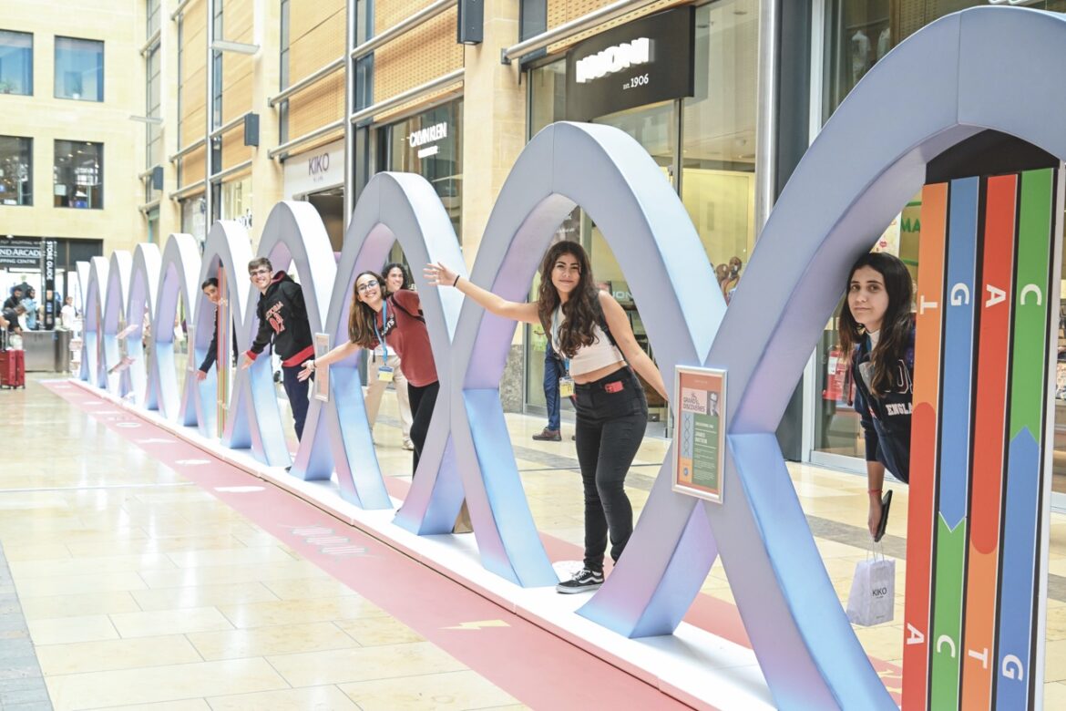 A row of teenagers poke their heads through a wave sculpture inside a shopping centre