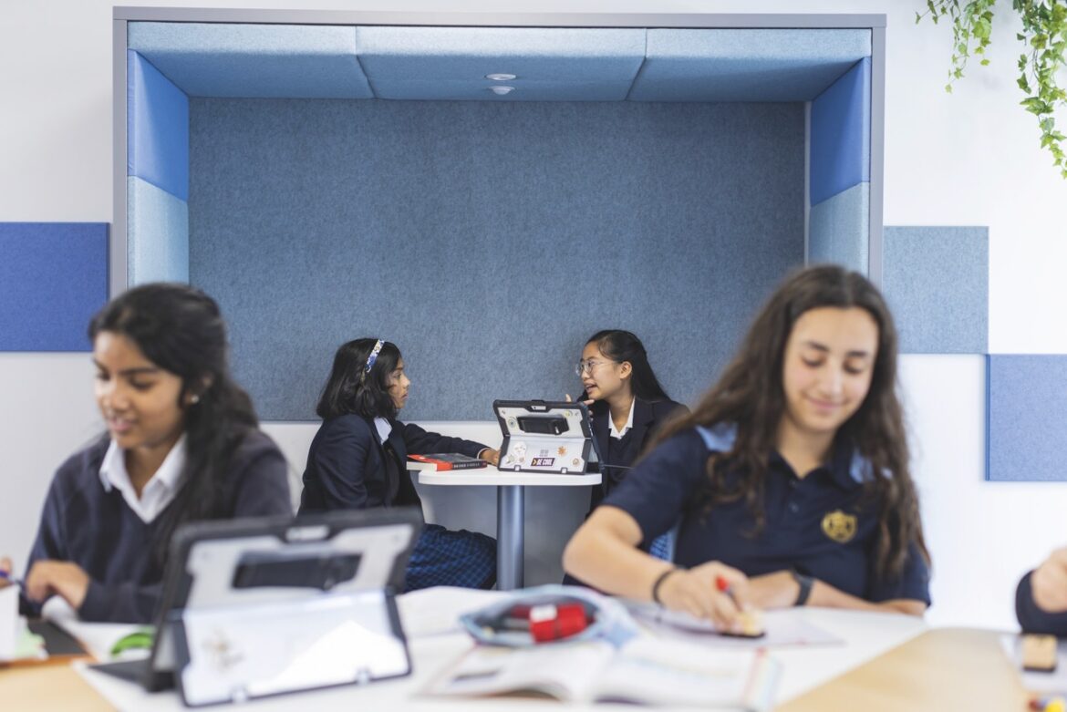 A classroom of girls in school uniform, working with tablets and talking