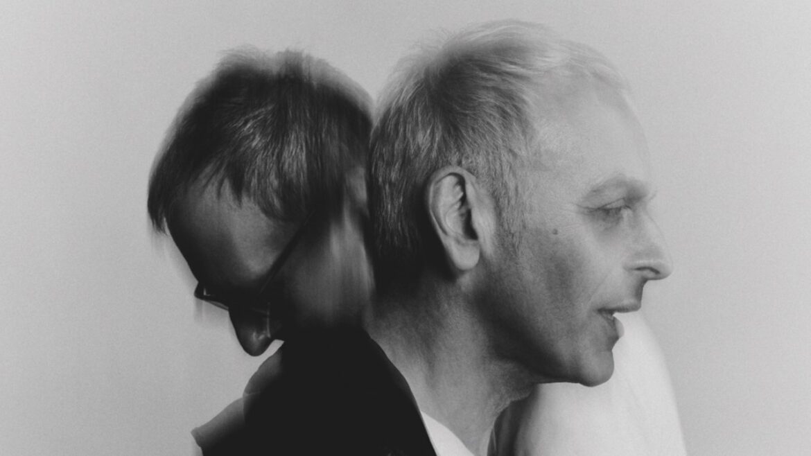 A greyscale image of two men. One faces to the right while the man behind faces the left. The image is slightly blurry