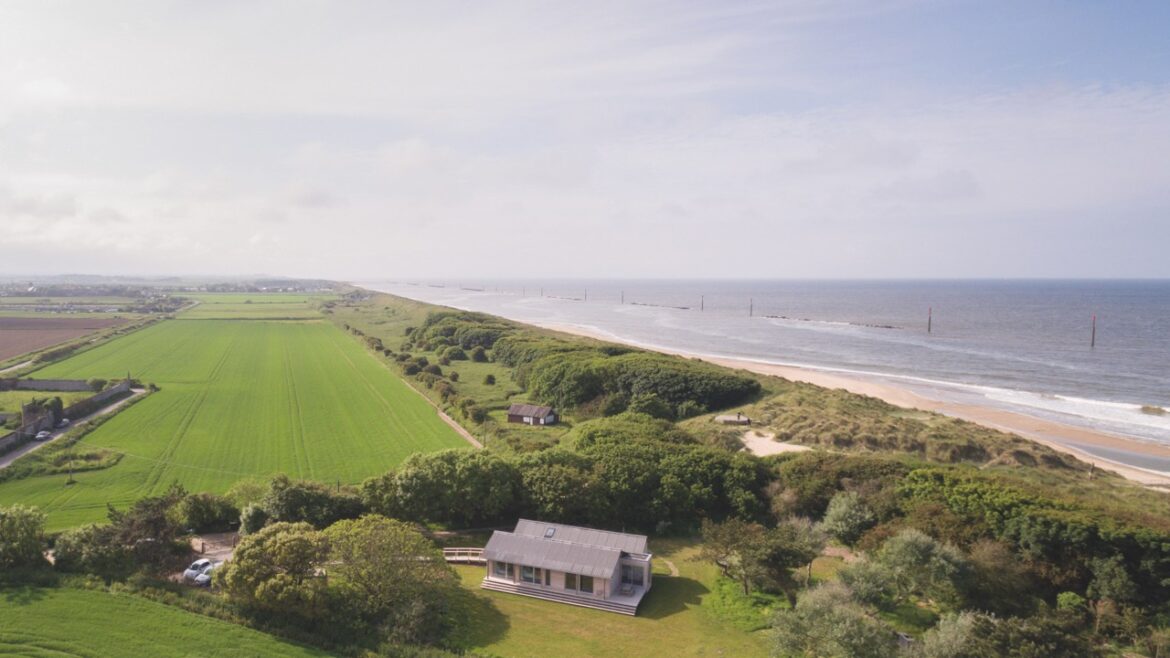 An aerial view of a modern house sheltered by trees, nearby to a beach