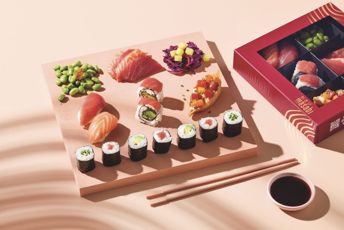An artistic photo of a board of sushi, next to chopsticks, a bowl of soy sauce and a box of more social