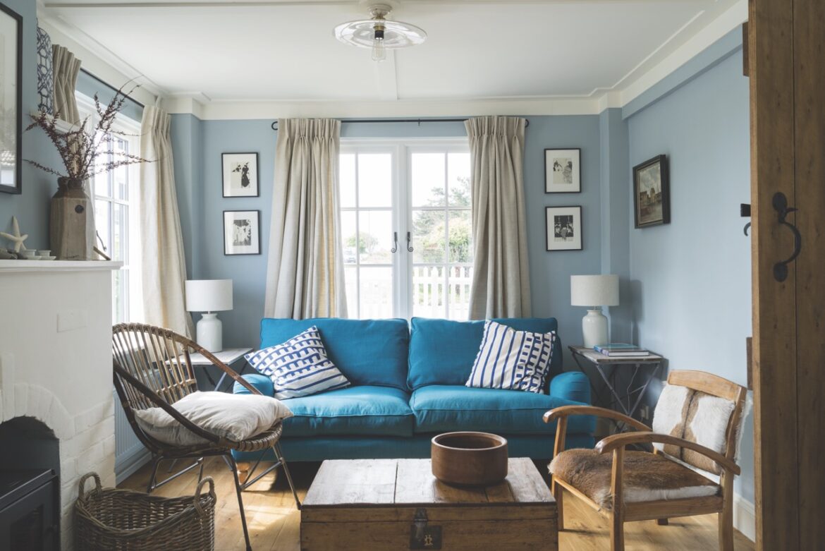 A blue living room using paint from Farrow & Ball. There is a long blue sofa in front of a window