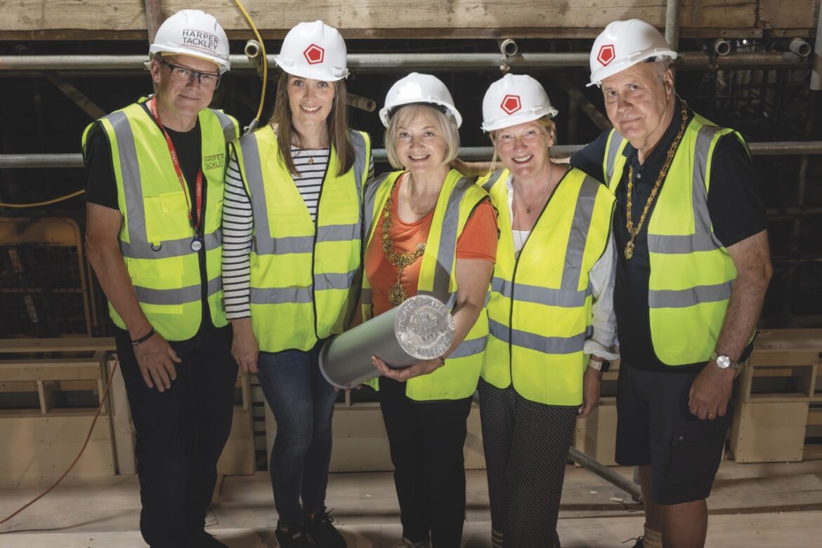 A team wearing hi-vis and helmets holding a time capsule in Cambridge Arts Theatre