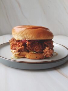 A chicken burger placed on a round plate on a marble table
