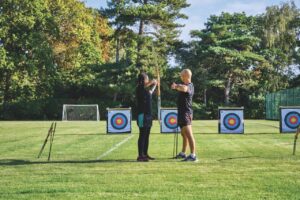 A student at Stephen Perse Cambridge practice archery with an instructor in an open field near targets