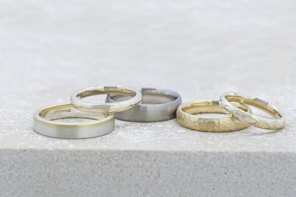 Harriet_Kelsall_Bespoke_Jewellery_Wedding-Feature (4) Large A line of different colour and shaped wedding rings by Harriet Kelsall Bespoke Jewellery sitting on a grey surface