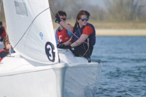 Teams of students at Kimbolton School sit on the side of a sailing boat in a lake