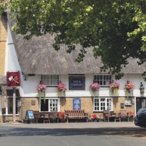 The exterior of the Axe and Compass pub in Cambridge with flower baskets and benches outside