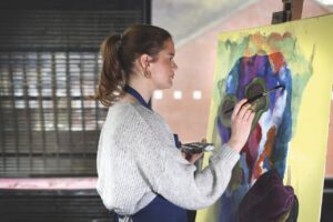 A student at Gresham's painting bright colours on a canvas while wearing an apron