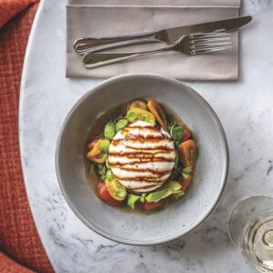Top view of a mozzarella salad next to cutlery and a glass of wine served by The Carpenters Arms