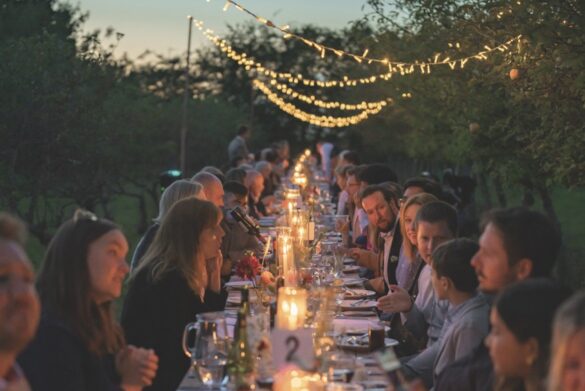 The Orchard Barn Ben Davis Wedding Photography . Large A long dinner table outside at Provenance Kitchen with people seated either side, candles down the middle and lights strewn overhead