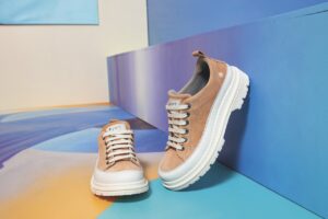 A pair of brown trainers on bright flooring. One leans vertically against a wall