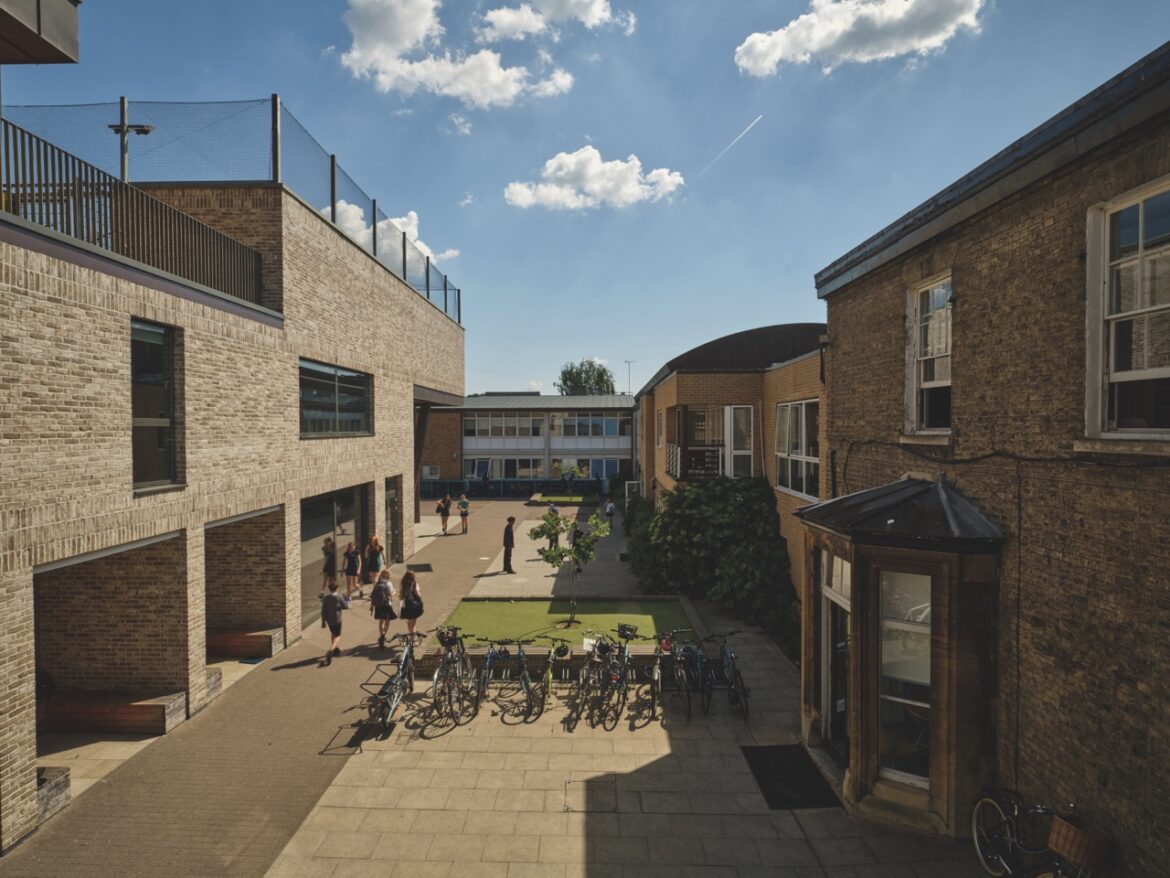 The exterior of the Stephen Perse Cambridge school with multiple brick buildings and students walking in the courtyard between